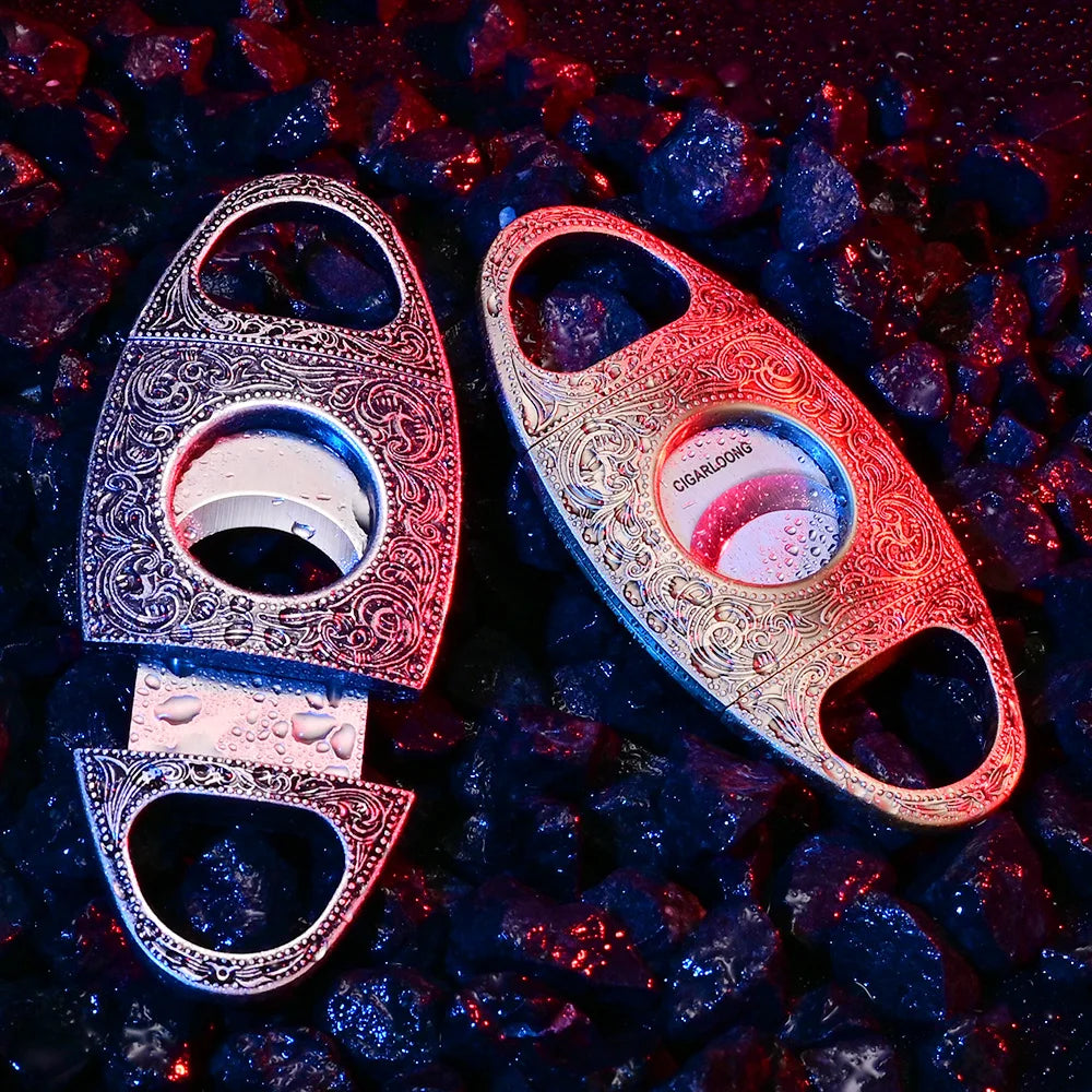 Two ornate cigar cutters on a dark, textured surface