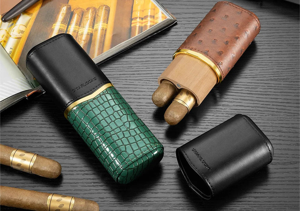 Three leather cigar cases in green, brown, and black on a dark surface with cigars.
