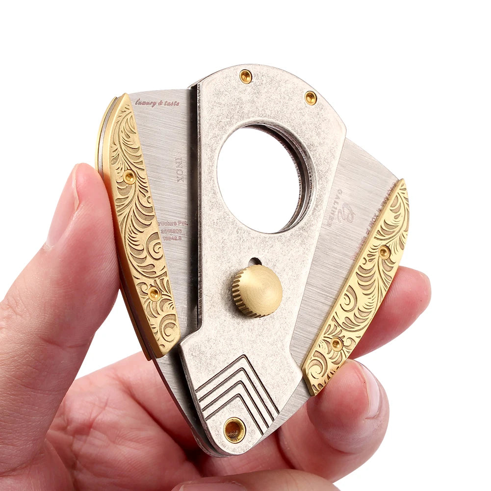 Cigar cutter with gold and silver design held in a hand against a white background
