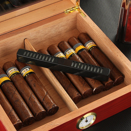 Open wooden humidor with cigars and a black cigar humidifier on a dark surface.