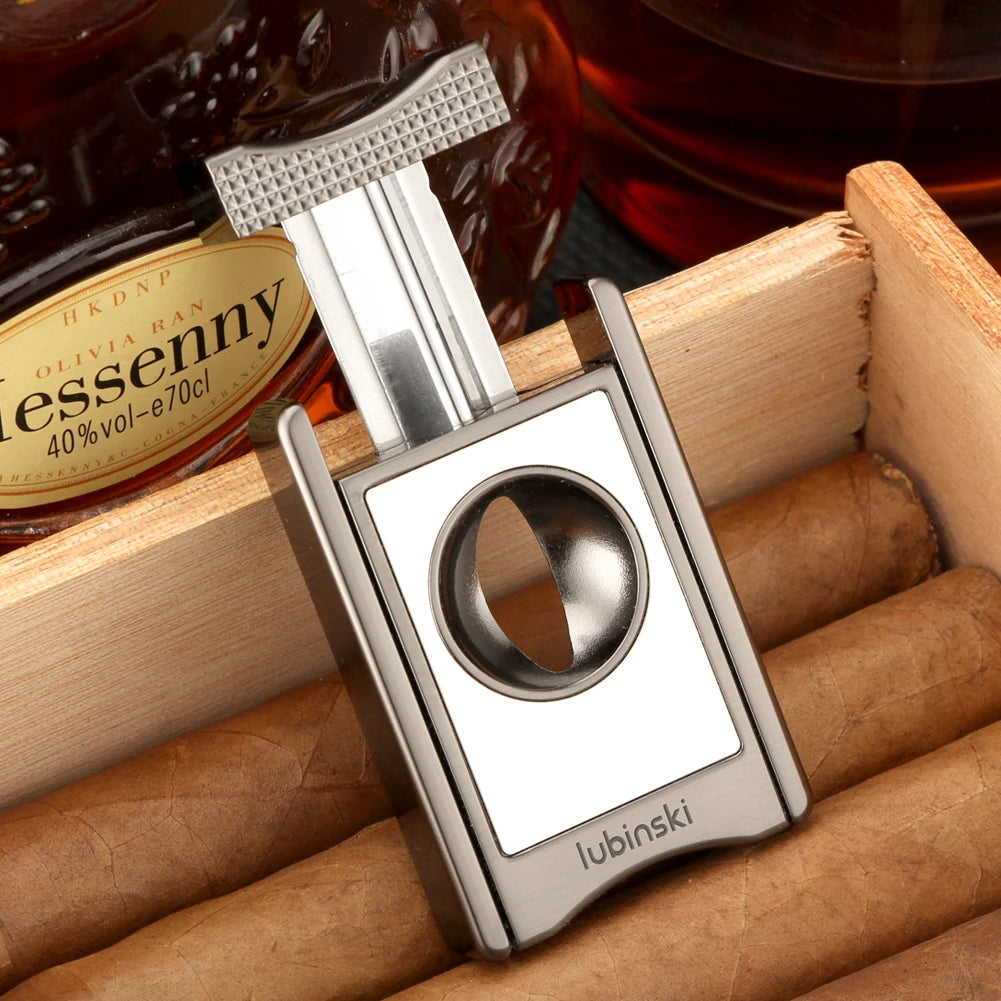 Cigar cutter  on a wooden tray with cigars and a bottle of liquor in the background.